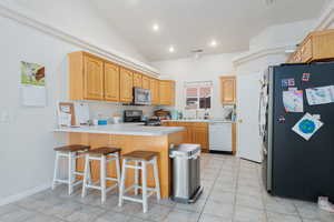 Kitchen featuring vaulted ceiling, light tile patterned flooring, appliances with stainless steel finishes, a kitchen breakfast bar, and kitchen peninsula