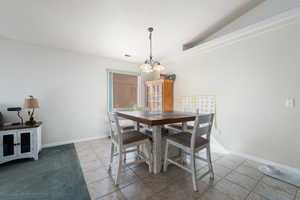 Dining room with vaulted ceiling, light tile patterned flooring, and a notable chandelier