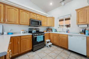 Kitchen with vaulted ceiling, appliances with stainless steel finishes, sink, and light tile patterned flooring