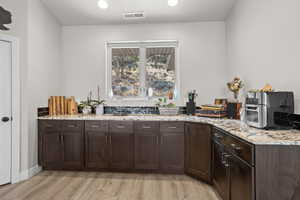 Kitchen featuring light stone counters, dark brown cabinets, and light hardwood / wood-style floors