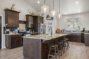 Kitchen with pendant lighting, appliances with stainless steel finishes, light stone countertops, and a kitchen island with sink