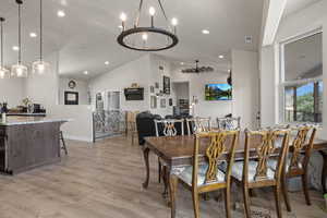 Dining space featuring vaulted ceiling, a notable chandelier, and light hardwood / wood-style flooring