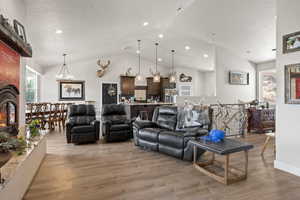 Living room featuring vaulted ceiling, a large fireplace, an inviting chandelier, and light wood-type flooring