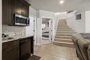 Kitchen featuring sink, dishwasher, dark brown cabinets, light stone counters, and a textured ceiling