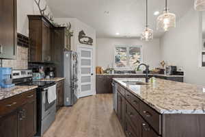 Kitchen with appliances with stainless steel finishes, pendant lighting, an island with sink, sink, and light hardwood / wood-style floors