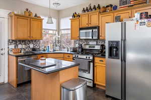 Kitchen with hanging light fixtures, stainless steel appliances, tasteful backsplash, a kitchen island, and dark tile patterned flooring