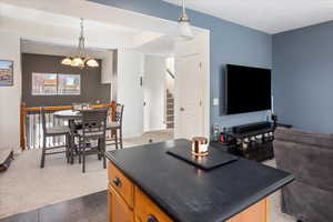 Kitchen with hanging light fixtures, a center island, a chandelier, and dark carpet