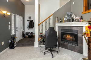 Carpeted home office featuring a tile fireplace and a high ceiling