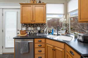 Kitchen with dark tile patterned flooring, dishwasher, sink, and decorative backsplash