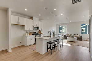 Kitchen with sink, appliances with stainless steel finishes, a kitchen breakfast bar, a kitchen island with sink, and white cabinets