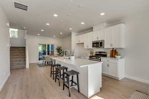 Kitchen with sink, a breakfast bar area, white cabinetry, stainless steel appliances, and a kitchen island with sink