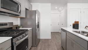 Kitchen with stainless steel appliances, gray cabinets, sink, and light hardwood / wood-style floors