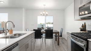 Kitchen with sink, gray cabinetry, stainless steel appliances, decorative light fixtures, and light wood-type flooring