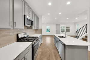 Kitchen featuring sink, light hardwood / wood-style flooring, gray cabinets, stainless steel appliances, and an island with sink