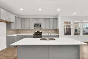 Kitchen featuring sink, gray cabinets, a kitchen island with sink, stainless steel appliances, and tasteful backsplash