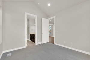 Unfurnished bedroom featuring light colored carpet, connected bathroom, and vaulted ceiling