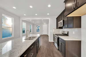 Kitchen featuring sink, dark brown cabinets, stainless steel appliances, light stone countertops, and dark hardwood / wood-style flooring