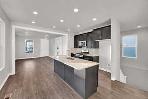 Kitchen featuring an island with sink, sink, stainless steel appliances, light stone countertops, and dark wood-type flooring