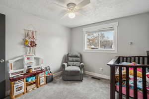 Bedroom with ceiling fan, carpet flooring, a textured ceiling, and a crib