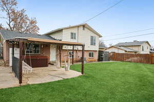 Rear view of property featuring a hot tub, a yard, central AC, and a patio area