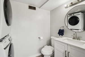 Bathroom with toilet, vanity, and stacked washing maching and dryer