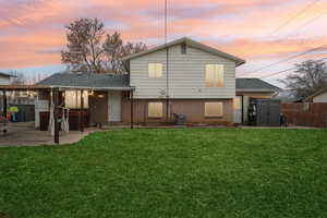 Back house at dusk featuring a lawn, a patio, and central air condition unit