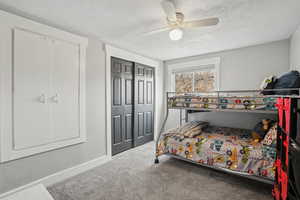 Carpeted bedroom with ceiling fan, a closet, and a textured ceiling