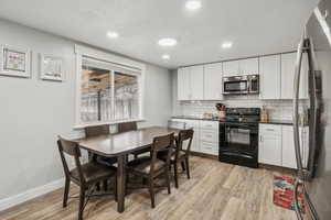 Kitchen with tasteful backsplash, light wood-type flooring, white cabinets, and appliances with stainless steel finishes