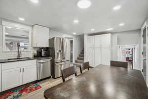 Kitchen with appliances with stainless steel finishes, tasteful backsplash, white cabinetry, sink, and light hardwood / wood-style flooring