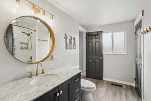 Bathroom featuring wood-type flooring, toilet, vanity, and a tile shower