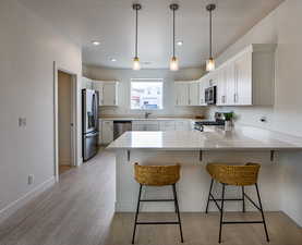 Kitchen featuring appliances with stainless steel finishes, white cabinetry, a kitchen bar, and kitchen peninsula