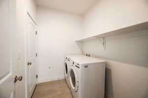 Clothes washing area featuring washing machine and clothes dryer and light hardwood / wood-style flooring