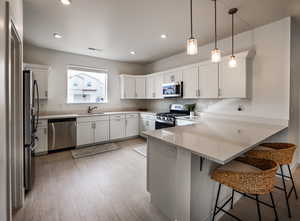 Kitchen with white cabinetry, kitchen peninsula, appliances with stainless steel finishes, and hanging light fixtures