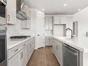 Kitchen featuring wall chimney exhaust hood, sink, light stone counters, appliances with stainless steel finishes, and an island with sink