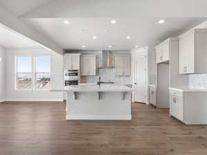 Kitchen with white cabinetry, a kitchen island with sink, wall chimney range hood, and dark hardwood / wood-style floors