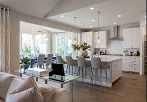Kitchen with decorative light fixtures, white cabinetry, a kitchen island with sink, dark wood-type flooring, and wall chimney exhaust hood