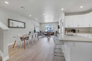 Kitchen with sink, a breakfast bar area, white cabinetry, light hardwood / wood-style flooring, and a textured ceiling