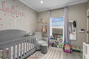 Bedroom featuring a crib, ornamental molding, and hardwood / wood-style flooring