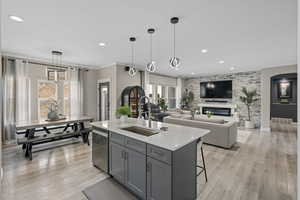 Kitchen featuring sink, gray cabinetry, hanging light fixtures, a center island with sink, and a fireplace