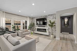 Living room with ornamental molding, a stone fireplace, and light hardwood / wood-style flooring