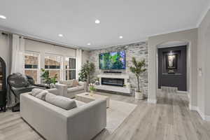 Living room with ornamental molding, light wood-type flooring, and a fireplace