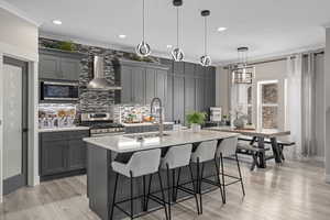 Kitchen featuring stainless steel appliances, hanging light fixtures, gray cabinetry, and wall chimney range hood