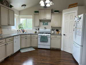 Kitchen with vaulted ceiling, cream cabinets, dark wood-type flooring, and white appliances