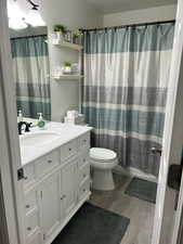 Full bathroom featuring hardwood / wood-style flooring, vanity, shower / tub combo with curtain, and toilet