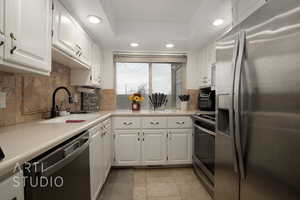 Kitchen with a raised ceiling, sink, white cabinets, decorative backsplash, and stainless steel appliances