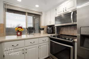 Kitchen with white cabinetry, stainless steel appliances, and backsplash