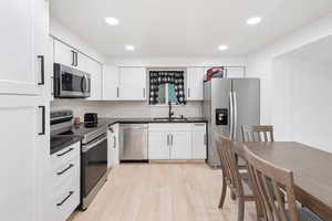 Kitchen featuring white cabinetry, appliances with stainless steel finishes, sink, and light wood-type flooring