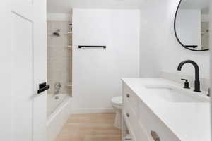 Full bathroom with vanity, hardwood / wood-style floors, tiled shower / bath, and toilet