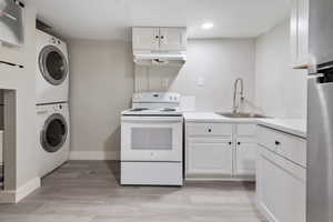 Kitchen featuring white electric range, stacked washer / drying machine, sink, white cabinetry, and light hardwood / wood-style floors