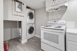 Kitchen featuring white range with electric cooktop, stacked washer / drying machine, light hardwood / wood-style flooring, and white cabinets